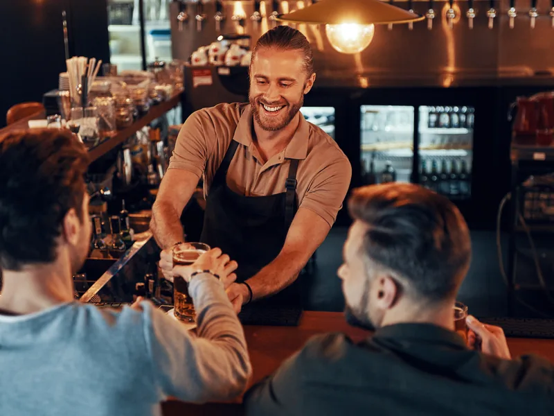 Bartender smiling as he hands a beer to a customer across the bar