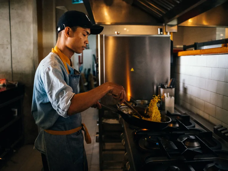 Line cook tossing rice in a pan on the stove in a restaurant kitchen